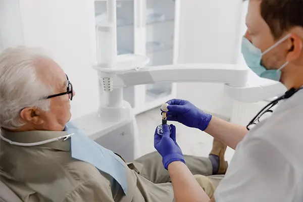 A dentist explains the dental implant process to an older patient with implant tooth model.